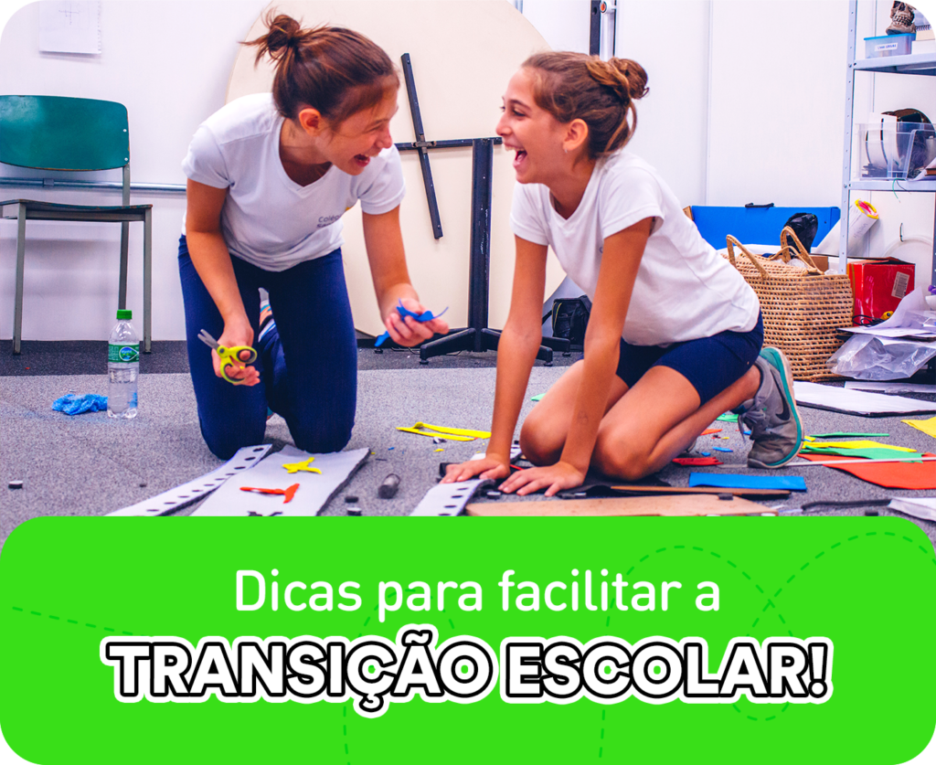 Duas crianças em fase de transição escolar no ambiente de aprendizagem, sorrindo e conversando ajoelhadas, enquanto estão com a mão na massa produzindo um trabalho manual.